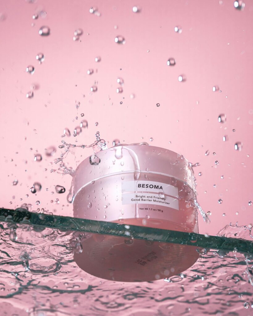 Vibrant beauty product splash with a moisturizer jar against a pink backdrop.